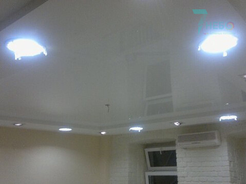 Белый глянцевый потолок с разными точечными светильниками и уровнями